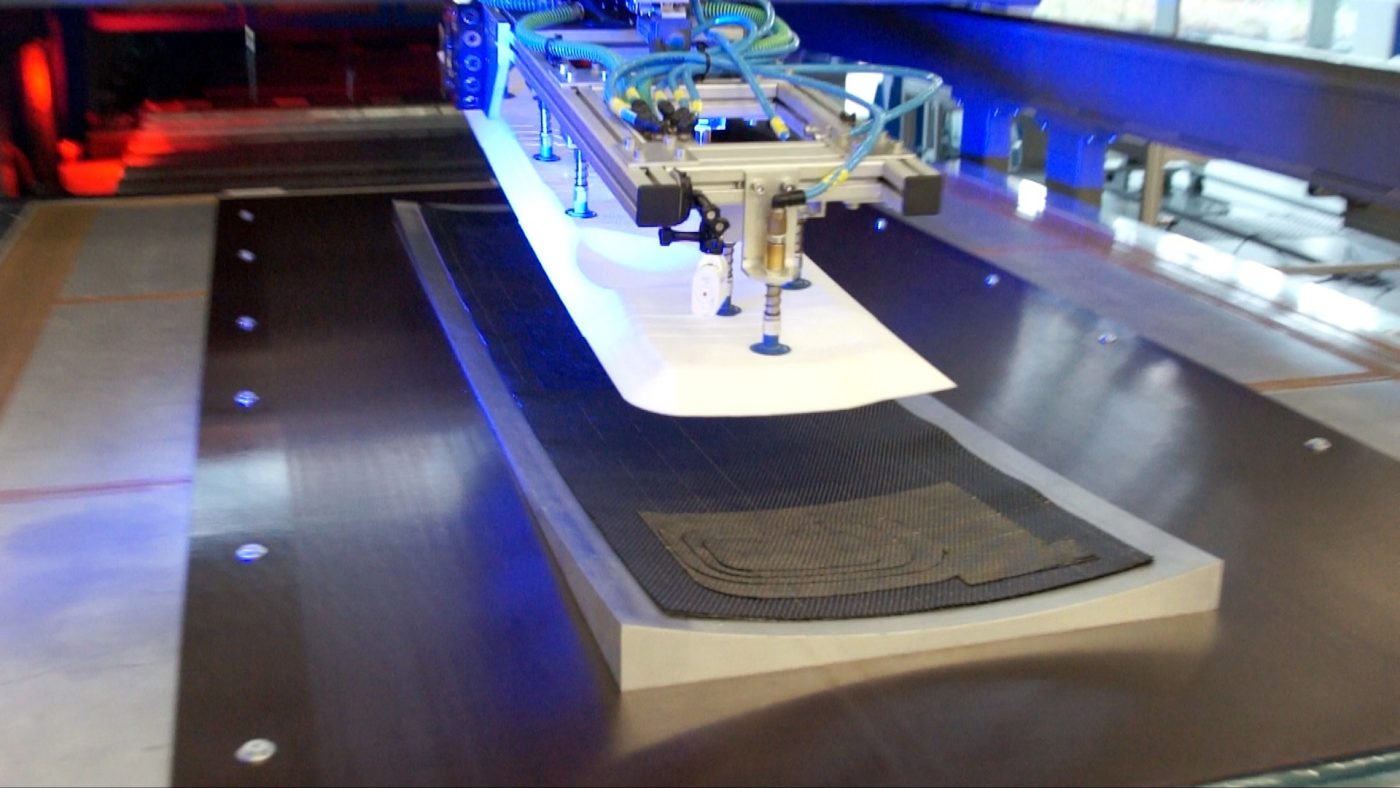 Automated machine with suction cups lifting a white sheet above a textured black surface.